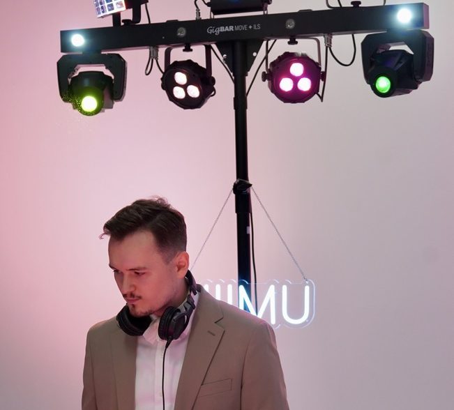 DJ an einem Mischpult in einem Eventraum mit Bühnenlichtern.