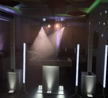Ein DJ steht an seinem Mischpult vor bunten Lichtern und einer beleuchteten Kulisse.