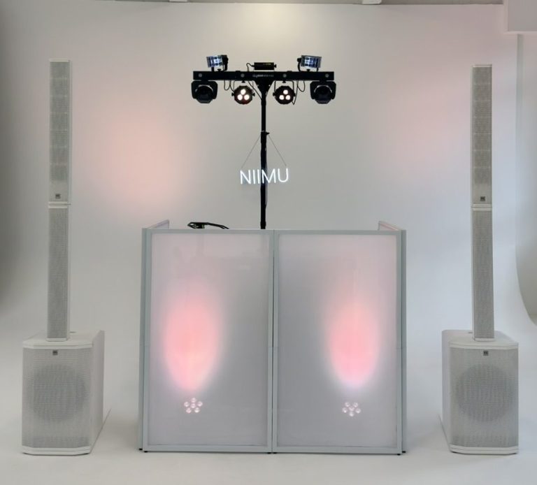 Ein DJ steht an seinem Mischpult vor bunten Lichtern und einer beleuchteten Kulisse.