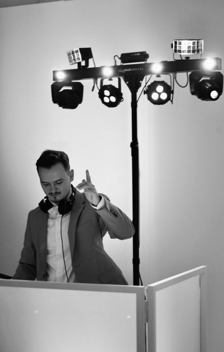 DJ steht an einem Mischpult mit bunten Lichtern und einer Aussicht auf die Stadt.