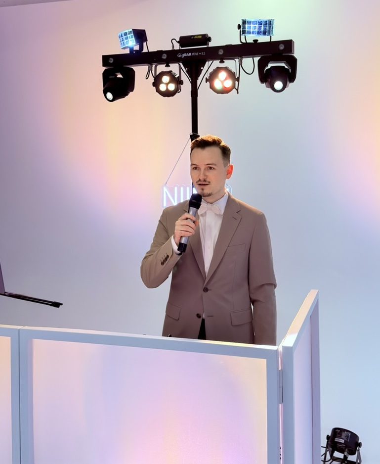 Mann mit kurzem, gestyltem Haar und einem lächelnden Gesicht, trägt einen hellen Anzug.